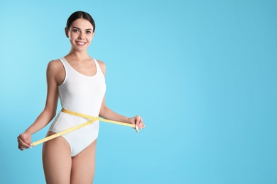 Photo of Attractive young woman with slim body measuring her waist on color background. Space for text