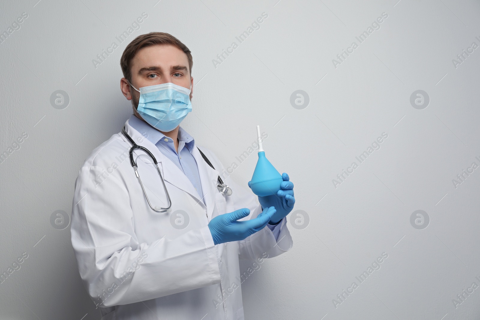 Photo of Doctor holding rubber enema on grey background. Space for text