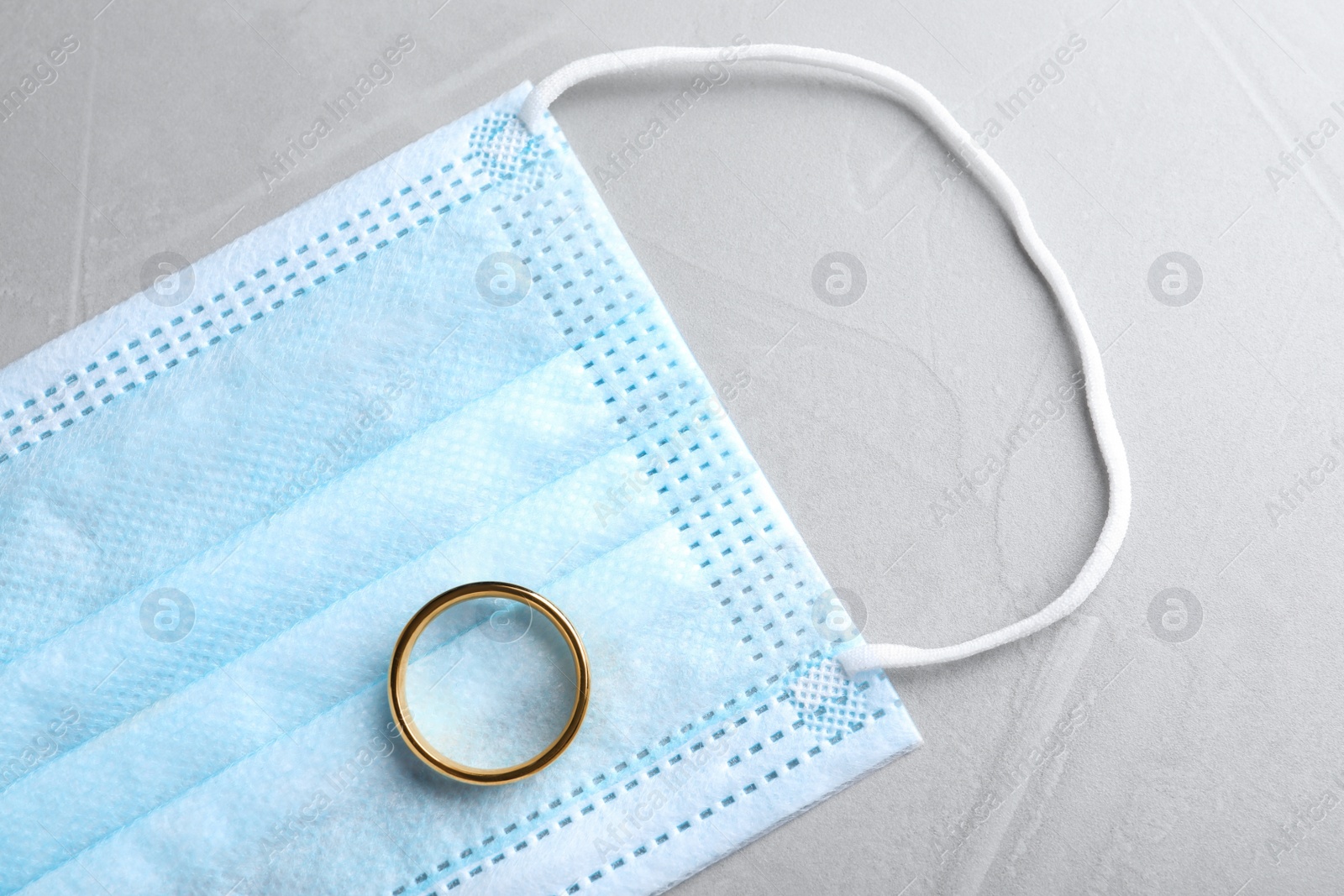 Photo of Protective mask and wedding ring on grey table, flat lay. Divorce during coronavirus quarantine