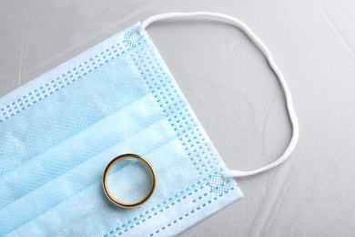 Protective mask and wedding ring on grey table, flat lay. Divorce during coronavirus quarantine