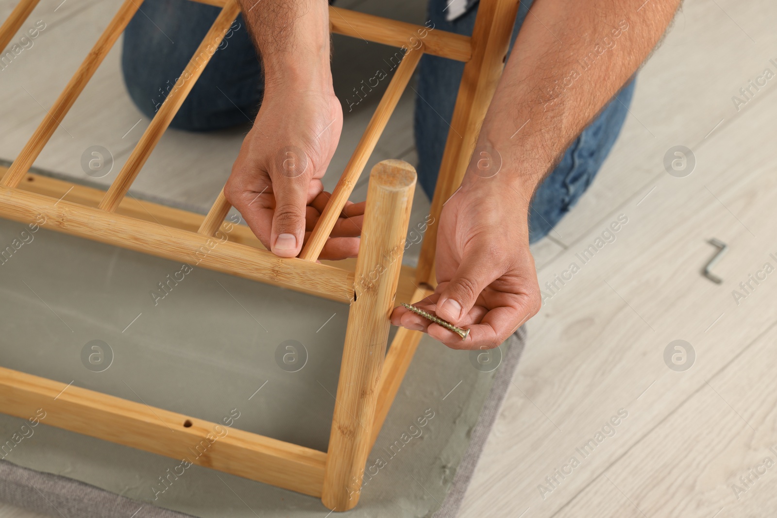 Photo of Man with self-tapping screw assembling furniture on floor, closeup