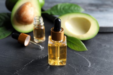 Photo of Bottle of essential oil and fresh avocado on black table