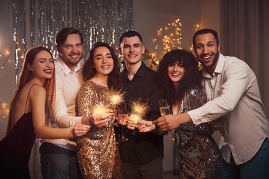 Photo of Happy friends with glasses of wine and sparklers celebrating birthday indoors