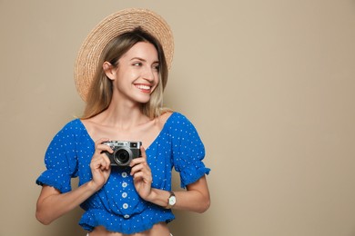 Beautiful young woman with straw hat and camera on beige background, space for text. Stylish headdress