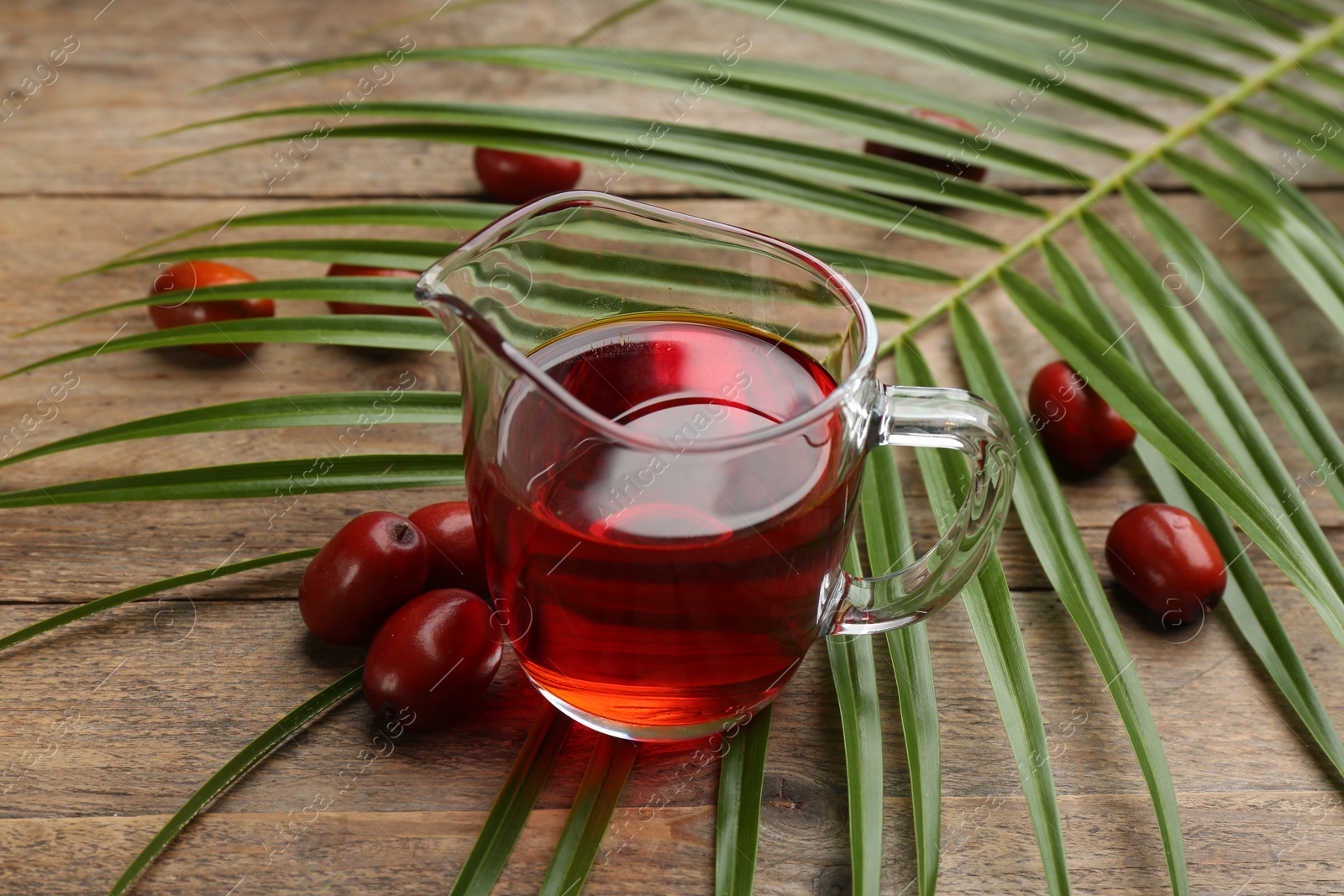 Photo of Palm oil in glass jug, tropical leaf and fruits on wooden table