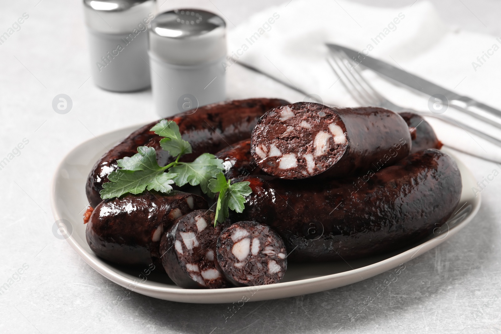 Photo of Tasty blood sausages with parsley served on light grey table, closeup