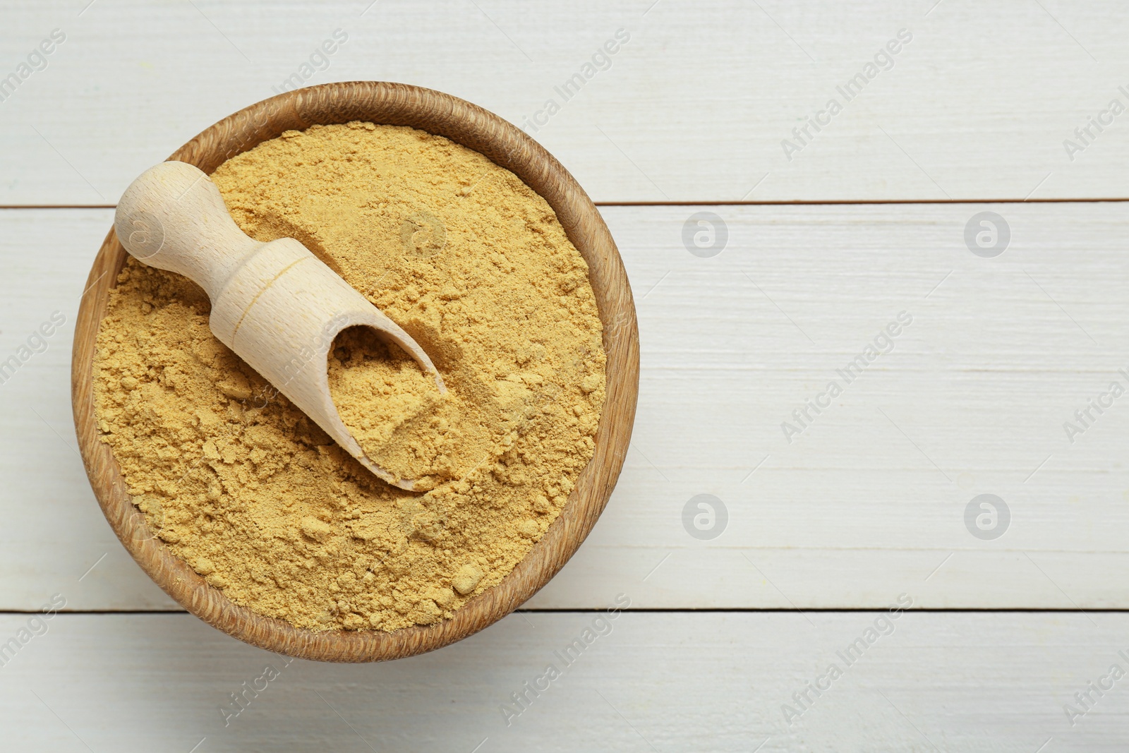 Photo of Bowl and scoop with aromatic mustard powder on white wooden table, top view. Space for text