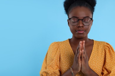 Photo of Woman with clasped hands praying to God on light blue background. Space for text