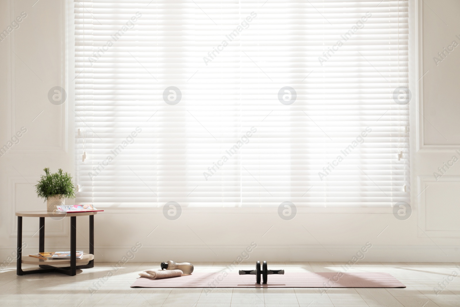 Photo of Exercise mat, ab roller, towel and bottle of water near window in spacious room