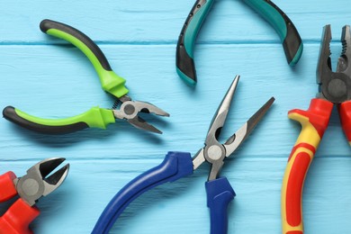 Different pliers on light blue wooden table, flat lay