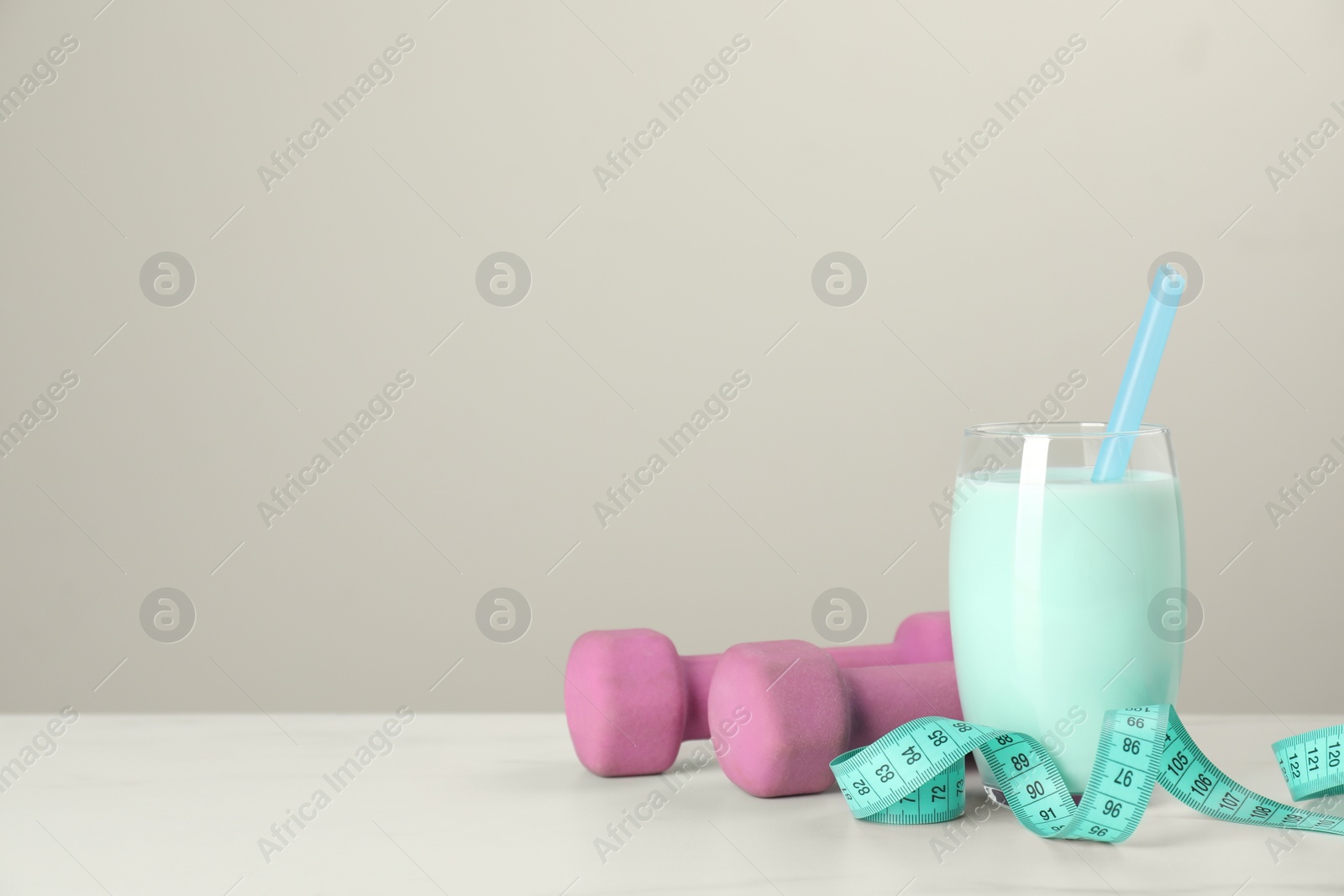 Photo of Tasty shake, dumbbells and measuring tape on white table against light gray background, space for text. Weight loss