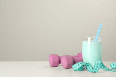 Photo of Tasty shake, dumbbells and measuring tape on white table against light gray background, space for text. Weight loss