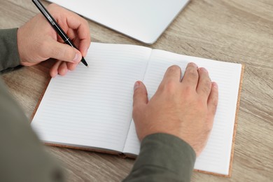 Young man writing in notebook at wooden table, closeup