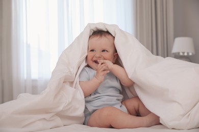 Photo of Cute little baby under soft blanket on bed at home
