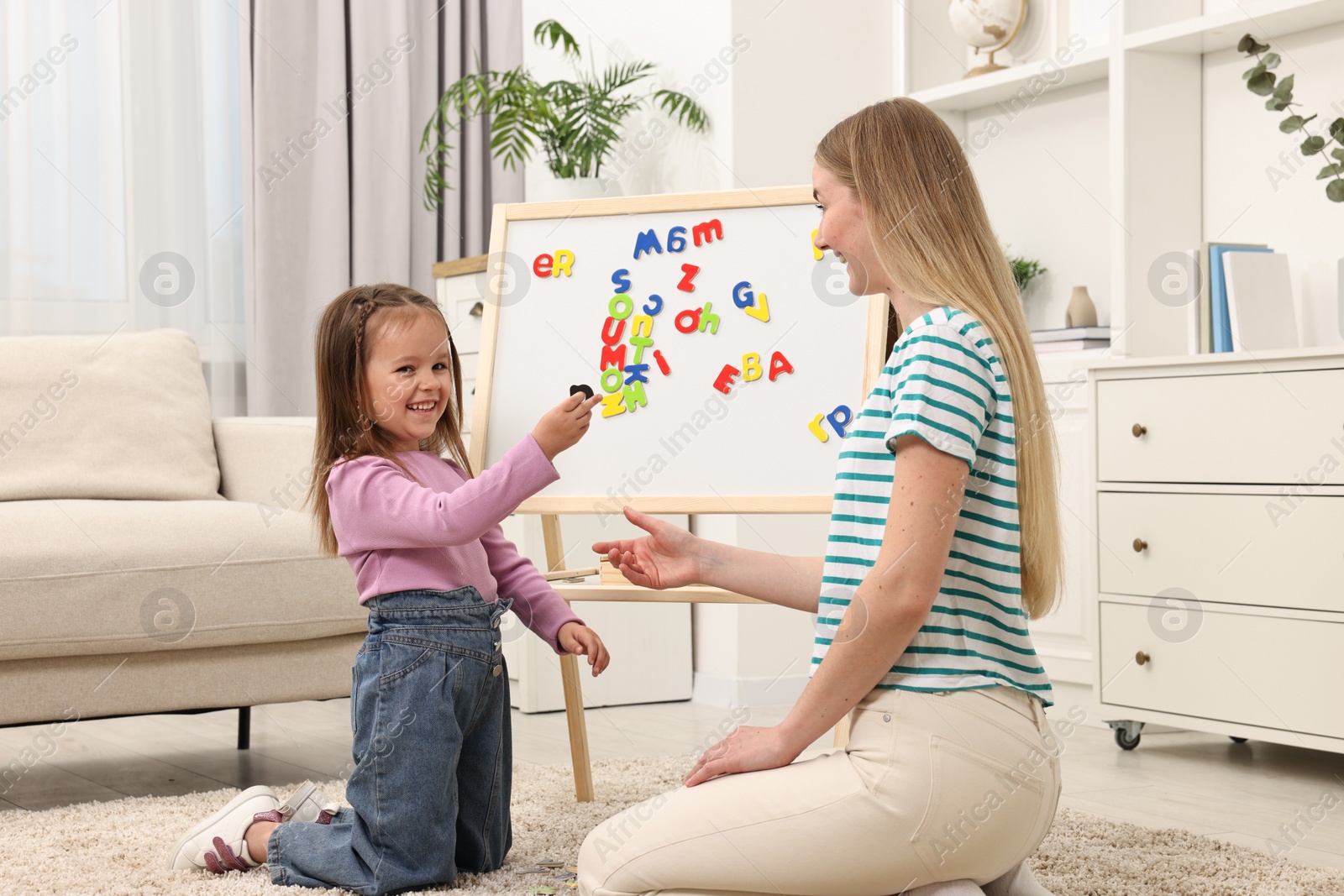 Photo of Mom teaching her daughter alphabet with magnetic letters at home