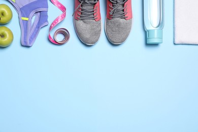 Flat lay composition with sneakers, measuring tape and sportswear on light blue background. Space for text