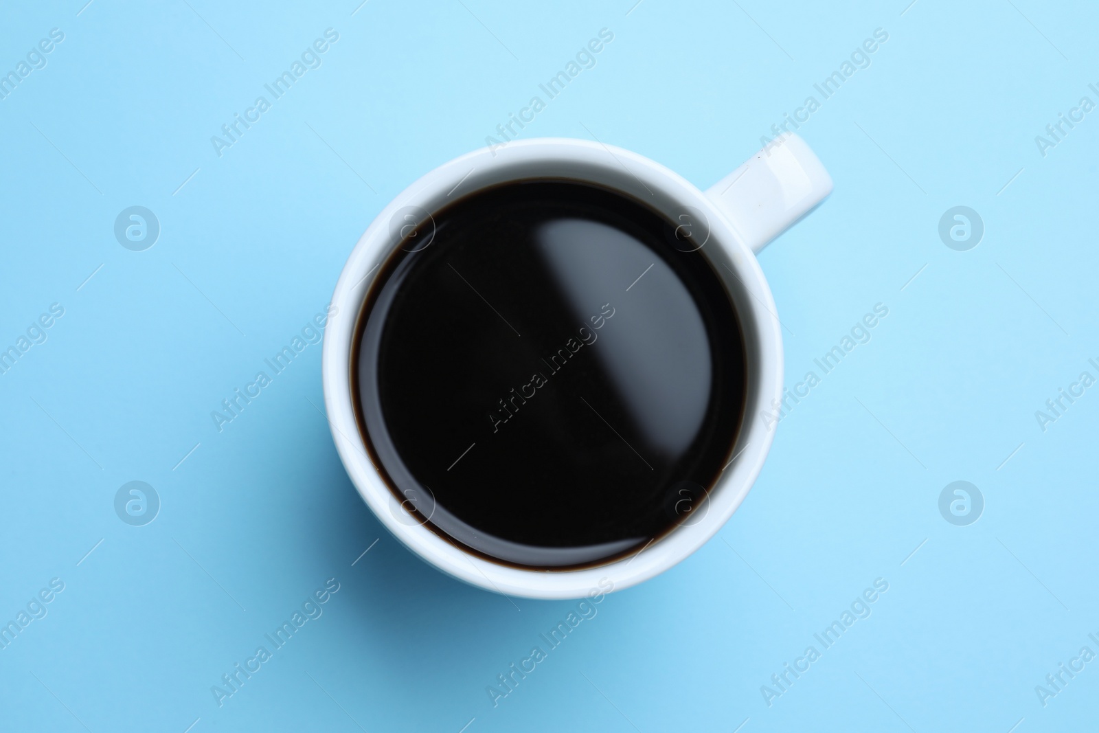 Photo of White mug of freshly brewed hot coffee on light blue background, top view