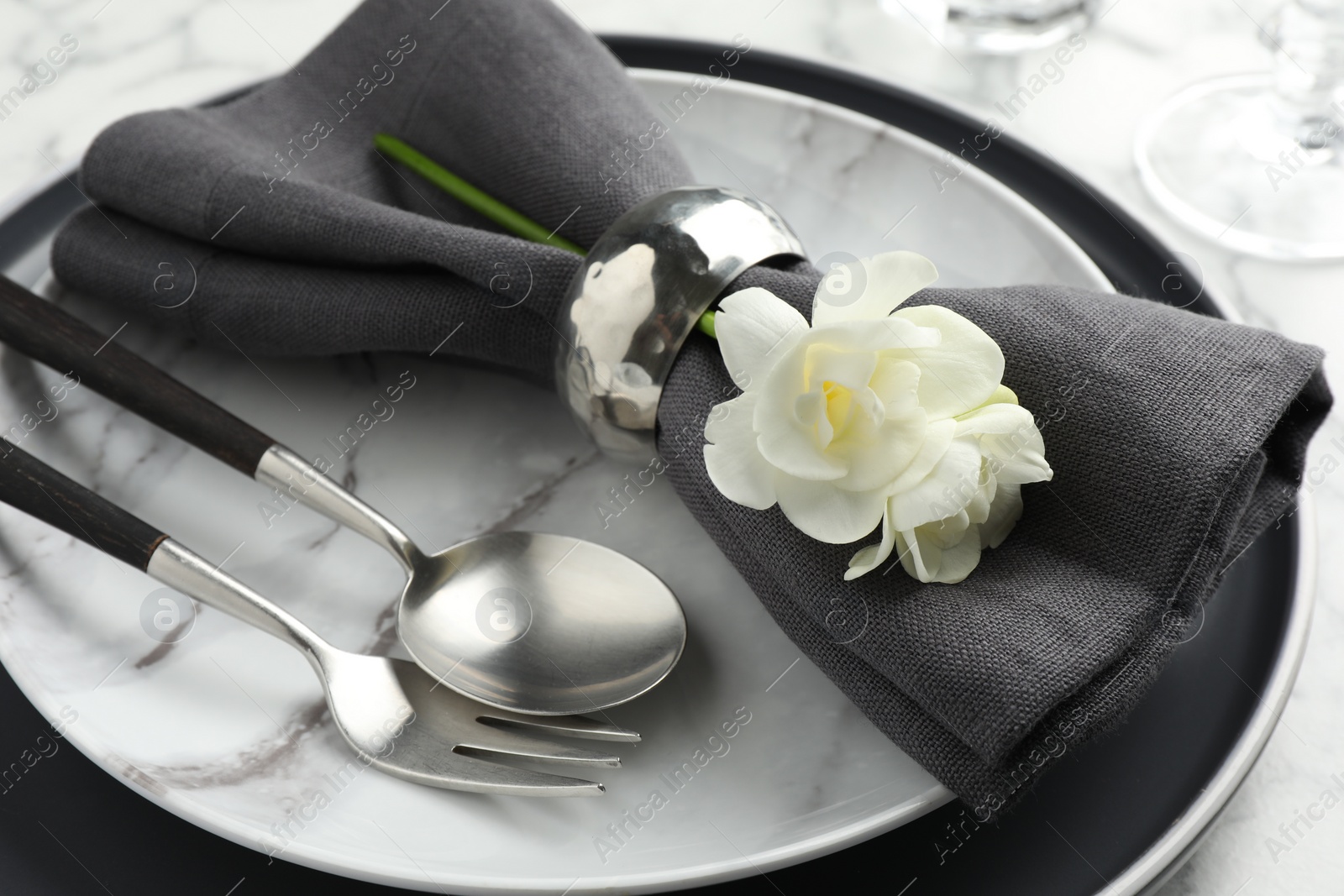 Photo of Stylish setting with cutlery, napkin, flowers and plates on white marble table, closeup