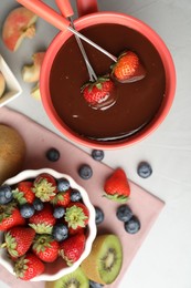 Photo of Dipping strawberries into fondue pot with chocolate on grey table, top view