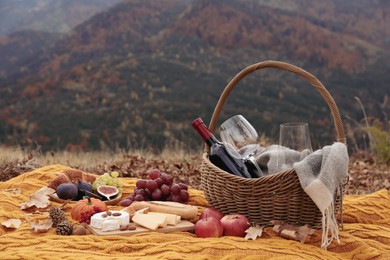 Photo of Knitted plaid with picnic basket, wine and snacks in mountains on autumn day, space for text