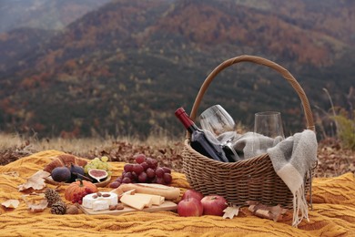 Knitted plaid with picnic basket, wine and snacks in mountains on autumn day, space for text