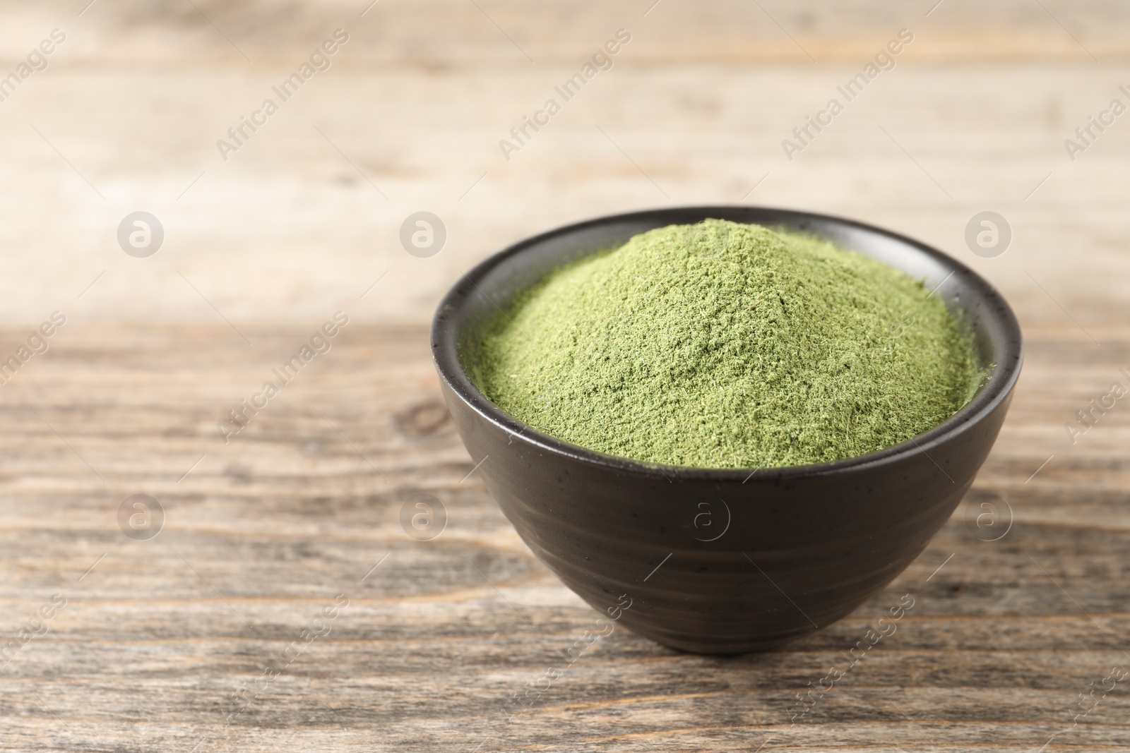 Photo of Wheat grass powder in bowl on wooden table, closeup. Space for text