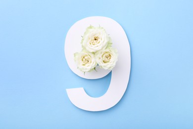 Photo of Paper number 9 and beautiful flowers on light blue background, top view
