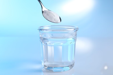 Photo of Adding baking soda into glass of water on light blue background