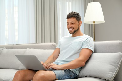 Photo of Happy man using laptop on sofa at home. Internet shopping