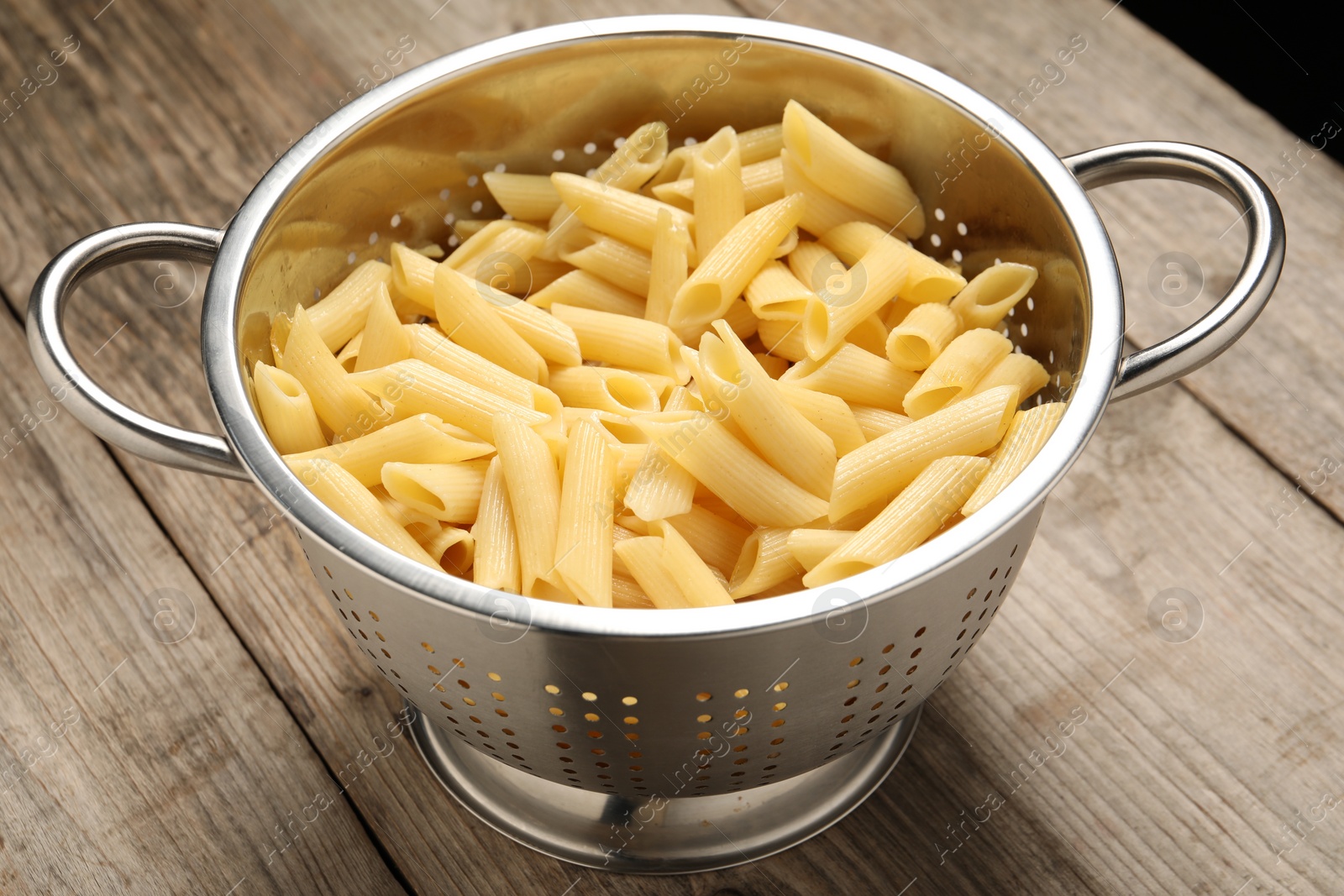 Photo of Delicious penne pasta in colander on wooden table, closeup