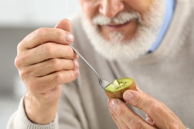Photo of Man eating kiwi with spoon on blurred background, closeup