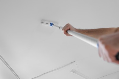 Photo of Handyman painting ceiling with roller, low angle view. Space for text