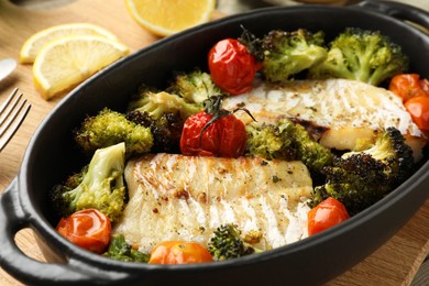 Photo of Tasty cod cooked with vegetables on wooden table, closeup