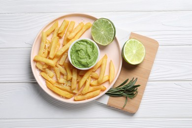 Tray with plate of french fries, avocado dip, lime and rosemary on white wooden table, top view