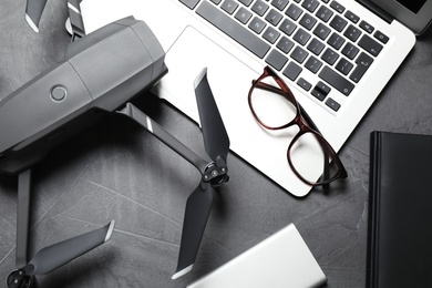 Photo of Modern drone with video camera and laptop on grey stone table, flat lay