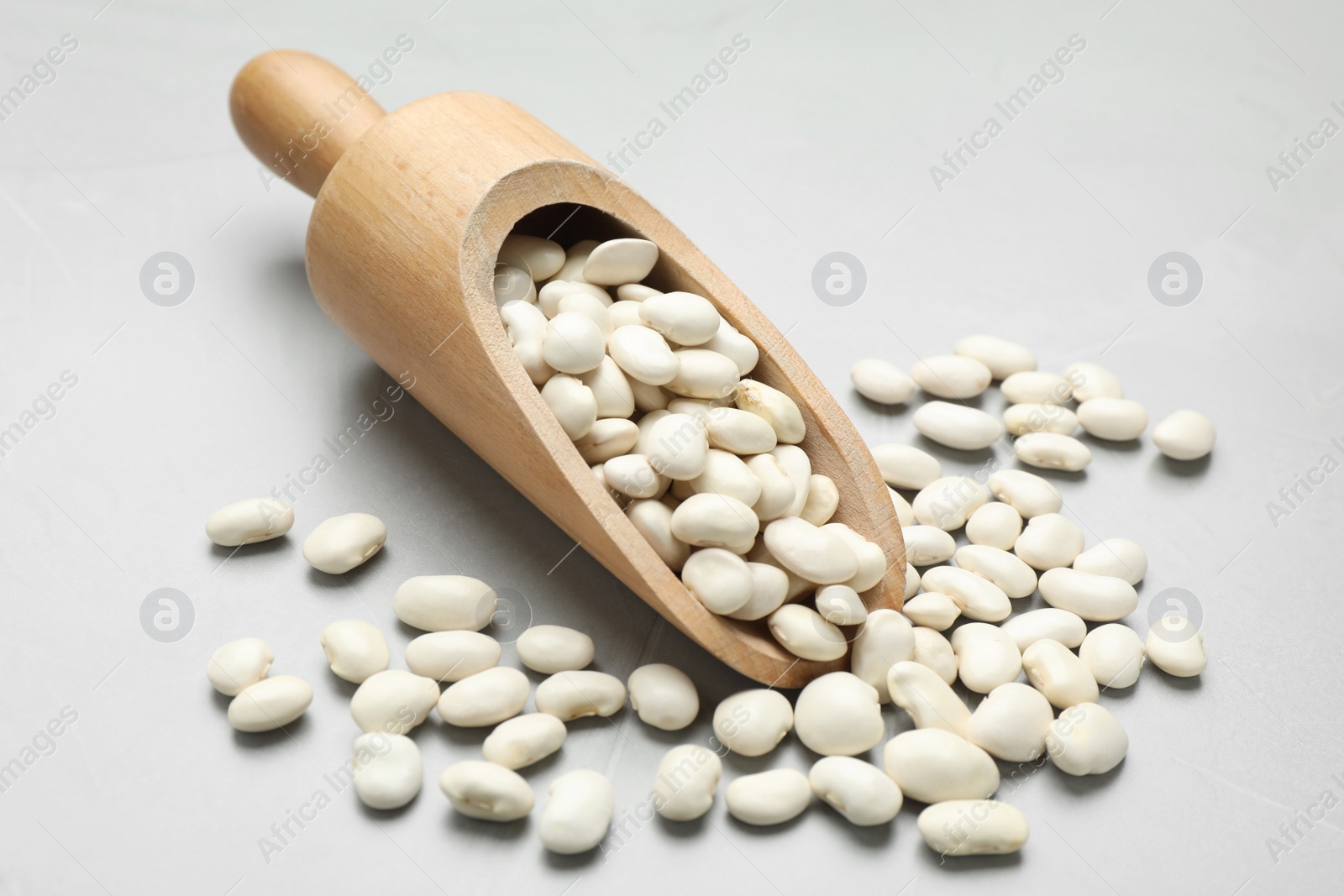 Photo of Wooden scoop with raw white beans on light grey table, closeup