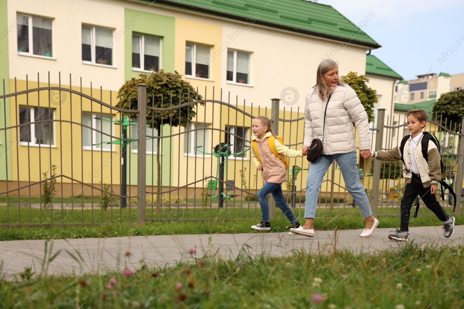 Photo of Being late for school. Senior woman and her grandchildren with backpacks running outdoors