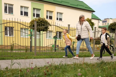 Photo of Being late for school. Senior woman and her grandchildren with backpacks running outdoors