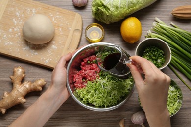 Photo of Woman adding soy sauce to gyoza filling at wooden table, top view