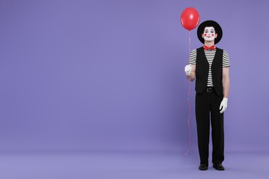 Photo of Funny mime artist with balloon on purple background. Space for text