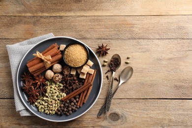 Plate with different aromatic spices and spoons on wooden table, flat lay. Space for text