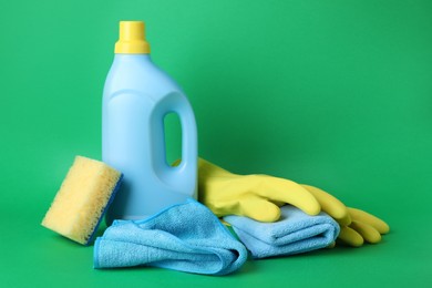 Photo of Microfiber cloths, sponge, rubber gloves and detergent on green background