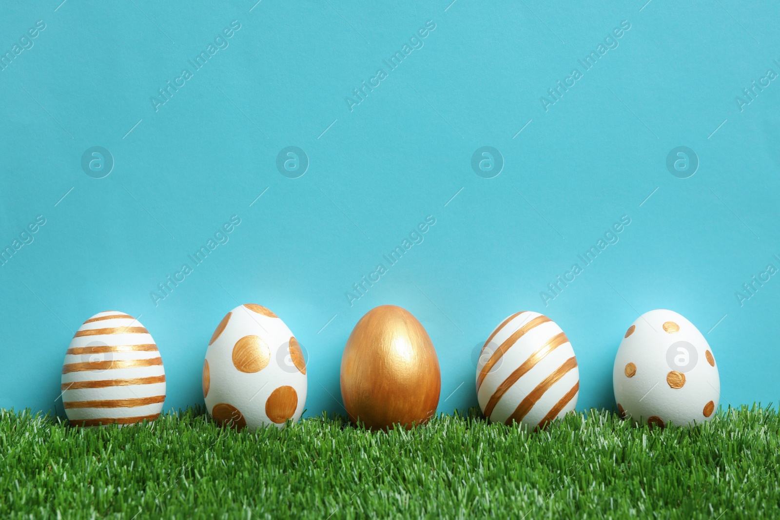 Photo of Line of traditional Easter eggs decorated with golden paint on green lawn against color background, space for text