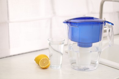 Photo of Water filter jug, glass and lemons on countertop in kitchen, space for text