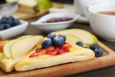 Fresh tasty puff pastry with jam, blueberries and pear on wooden table, closeup
