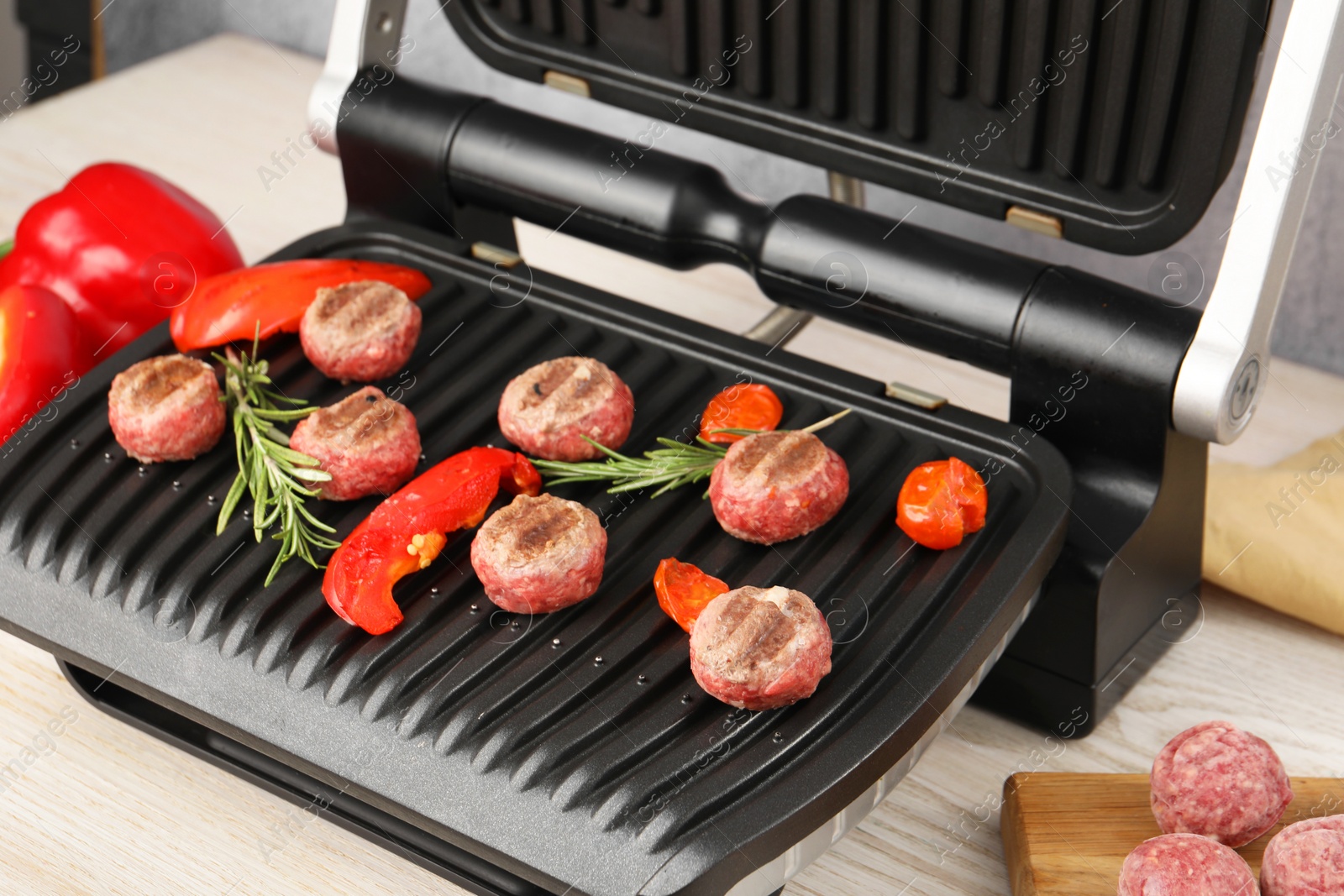 Photo of Electric grill with vegetables, meat balls and rosemary on table, closeup