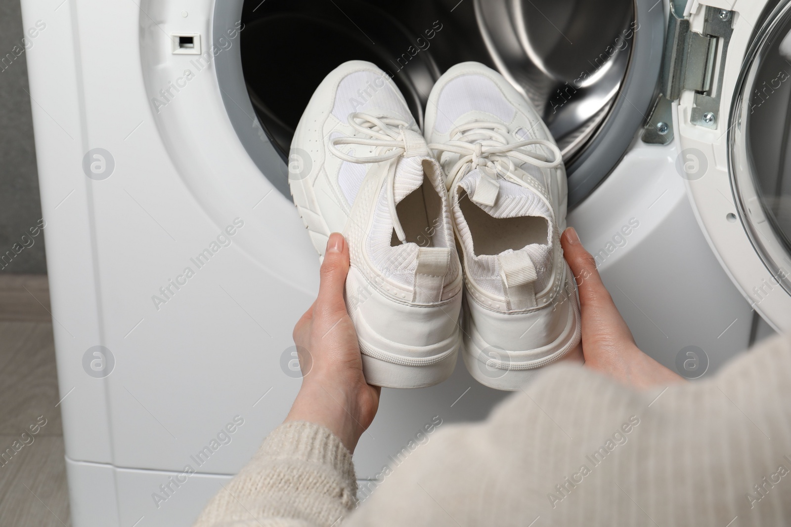 Photo of Woman putting stylish sneakers into washing machine, closeup