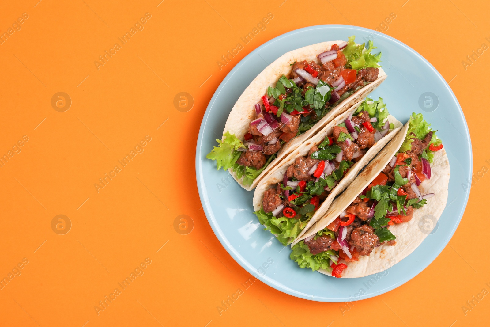 Photo of Delicious tacos with meat and vegetables on orange table, top view. Space for text