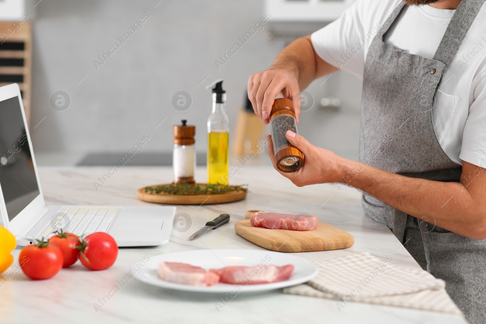 Photo of Man making dinner while watching online cooking course via laptop in kitchen, closeup