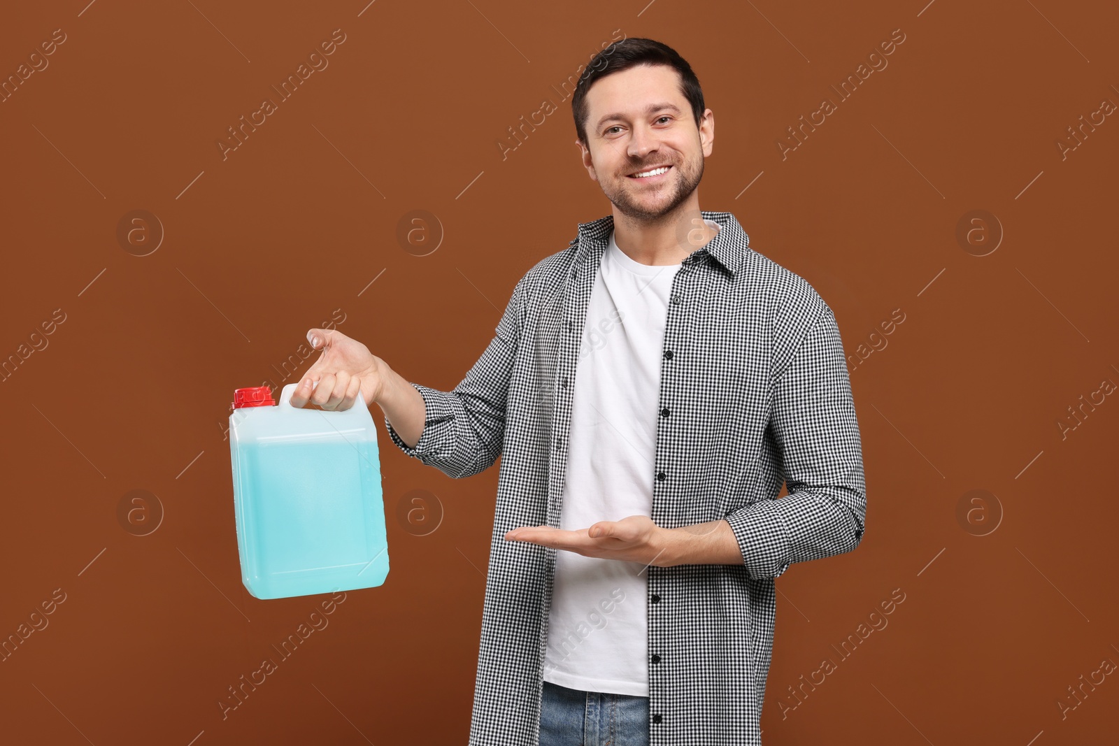 Photo of Handsome man showing canister with blue liquid on brown background